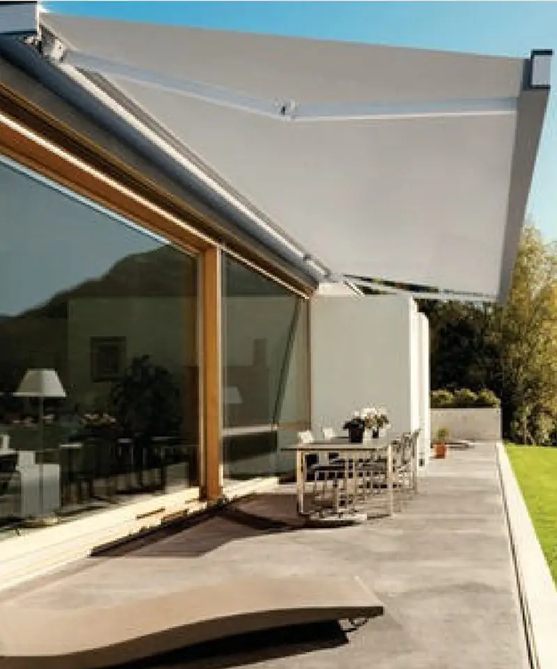 Varanda com toldo de braços articulados sobre uma mesa de jantar externa, com esquadrias de madeira e jardim ao fundo.